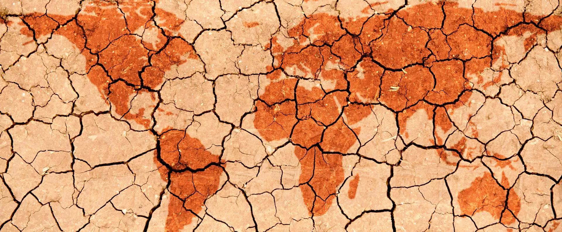 A world map rendered in faded red-brown, breaking apart across a parched, cracked earth surface.