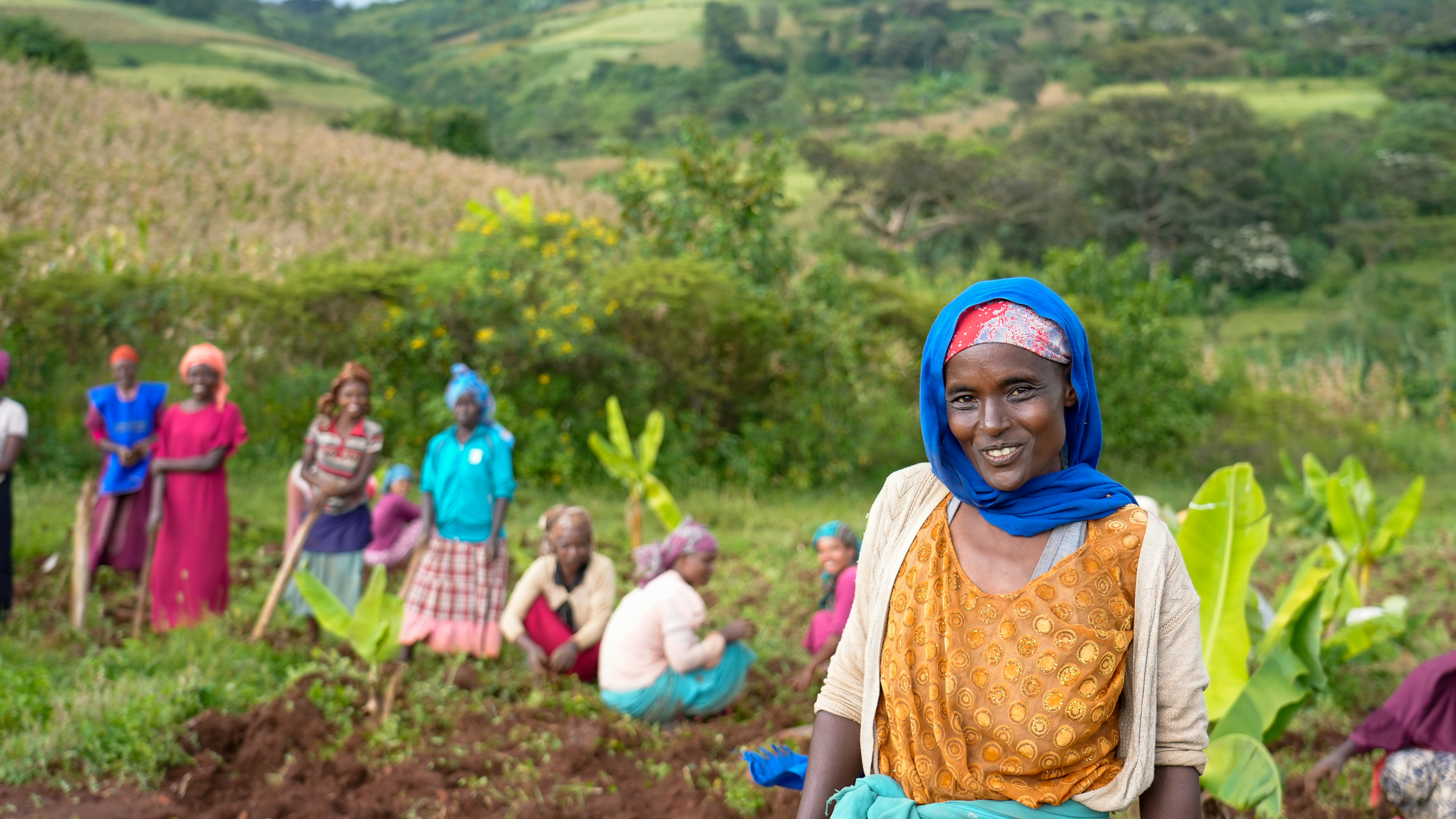 Portrait of Amina, leader of a women's collective in Jimma, Ethiopia, proudly standing in front of her community members engaged in agroforestry and land restoration activities.
