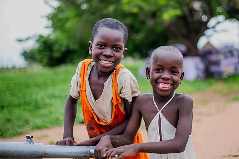 Two young girls share a joyful moment at a community water pump in northern Ghana